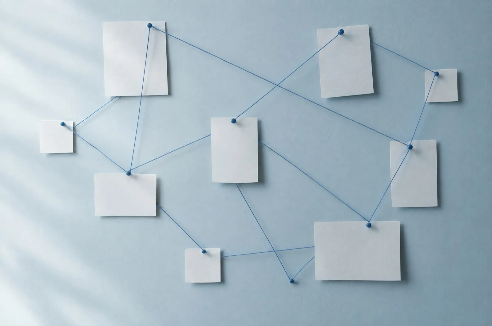 Paper cards pinned to a pale blue wall, connected by blue threads